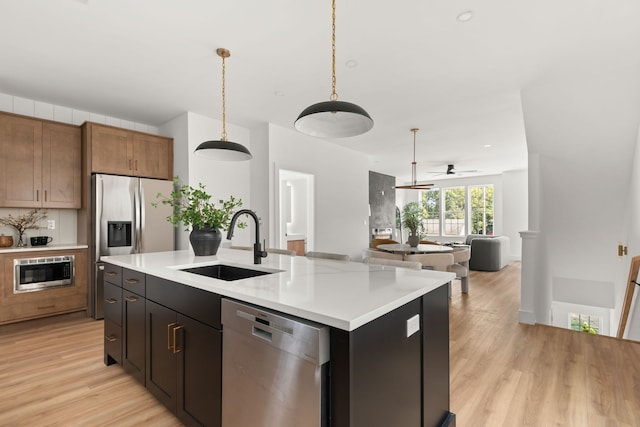 kitchen featuring sink, decorative light fixtures, a center island with sink, stainless steel appliances, and light hardwood / wood-style floors