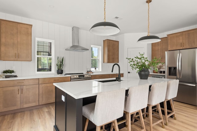 kitchen featuring pendant lighting, sink, a center island with sink, wall chimney range hood, and stainless steel appliances