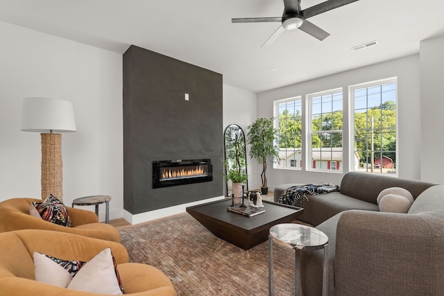 living room featuring ceiling fan, a large fireplace, and wood-type flooring