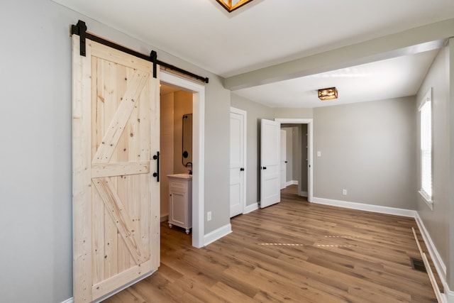 unfurnished bedroom with ensuite bathroom, hardwood / wood-style flooring, a barn door, and sink