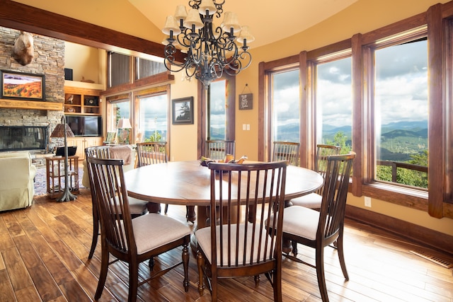 dining area with hardwood / wood-style flooring, vaulted ceiling, a chandelier, and a stone fireplace