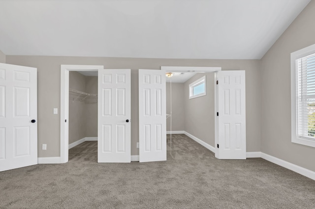 unfurnished bedroom with light colored carpet, a closet, vaulted ceiling, and a spacious closet