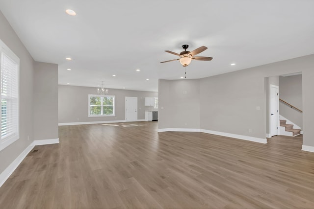 unfurnished living room with ceiling fan with notable chandelier and light hardwood / wood-style flooring