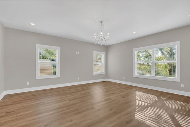 spare room featuring a wealth of natural light, an inviting chandelier, and wood-type flooring