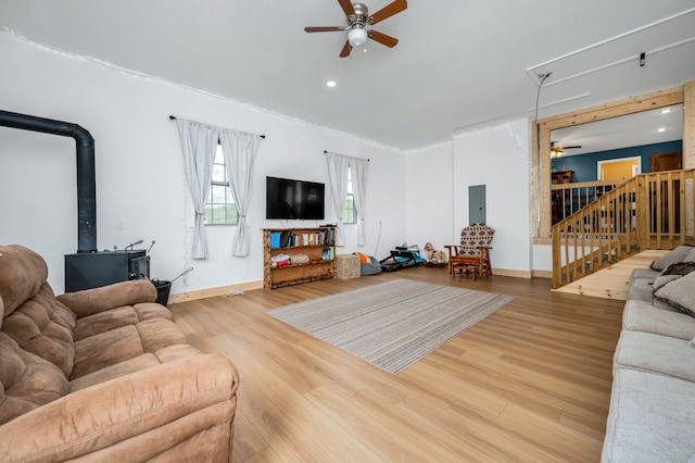 living room with a wood stove, electric panel, ceiling fan, and light hardwood / wood-style flooring