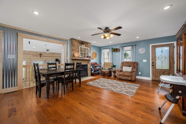 dining area featuring wood-type flooring, a stone fireplace, and ceiling fan