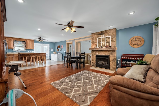 living room with sink, ceiling fan, a stone fireplace, and light hardwood / wood-style floors