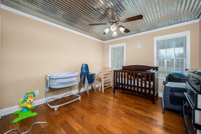 bedroom featuring wood-type flooring, a crib, ornamental molding, and ceiling fan