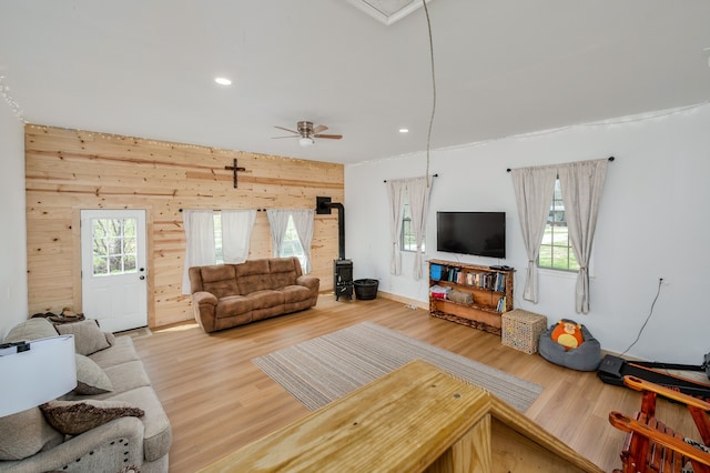 living room featuring a wood stove, wood-type flooring, ceiling fan, and a healthy amount of sunlight