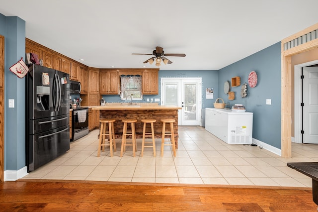 kitchen with light wood-type flooring, a kitchen island, ceiling fan, a breakfast bar area, and appliances with stainless steel finishes