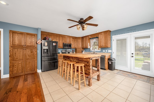 kitchen with light tile patterned flooring, french doors, appliances with stainless steel finishes, a breakfast bar area, and butcher block counters