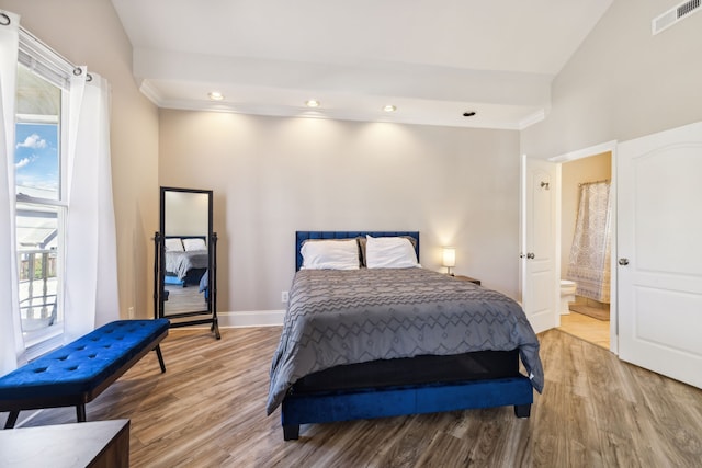 bedroom featuring vaulted ceiling, connected bathroom, and light hardwood / wood-style flooring