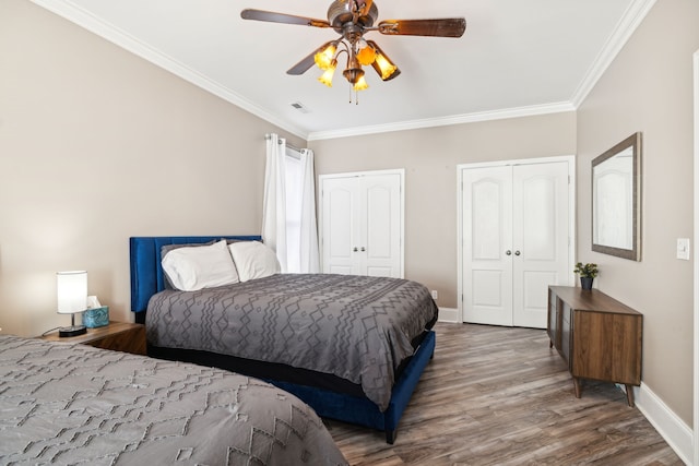 bedroom featuring ceiling fan, wood-type flooring, ornamental molding, and multiple closets