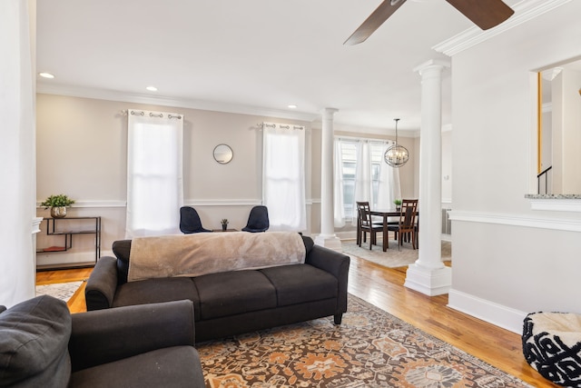 living room featuring ceiling fan with notable chandelier, light wood-type flooring, ornamental molding, and ornate columns