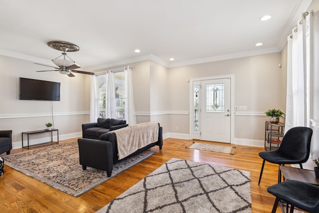 living room with a wealth of natural light, ceiling fan, ornamental molding, and light wood-type flooring