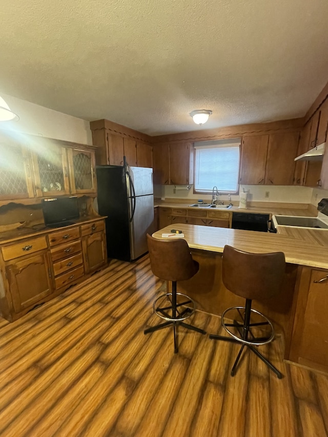 kitchen featuring stove, light wood-type flooring, a breakfast bar, sink, and stainless steel refrigerator