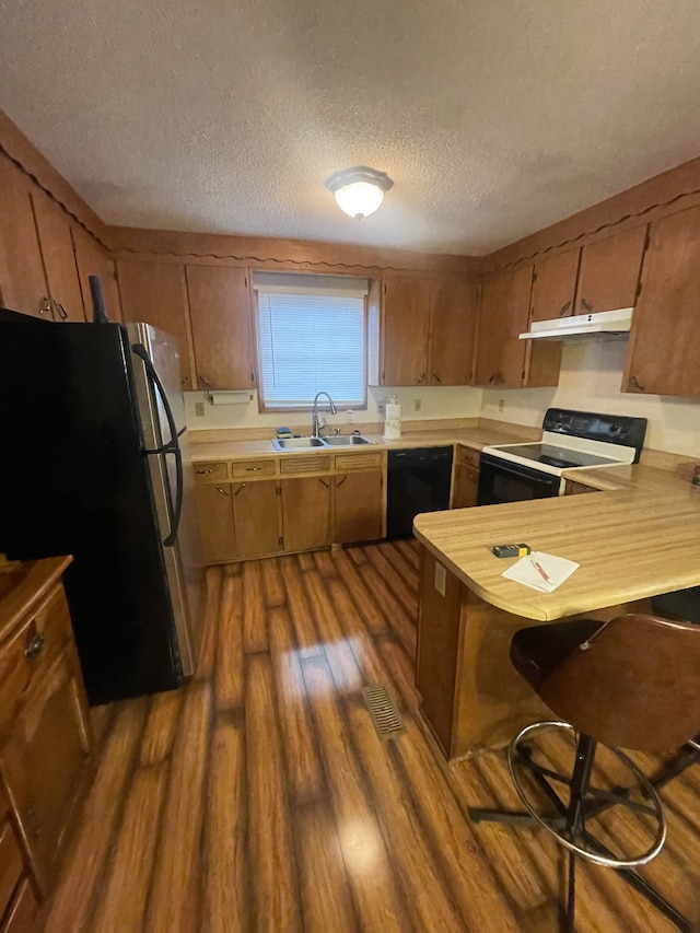 kitchen with kitchen peninsula, a textured ceiling, sink, black appliances, and dark hardwood / wood-style floors