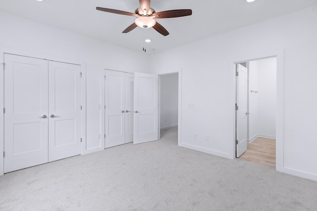 unfurnished bedroom with light carpet, ceiling fan, and two closets