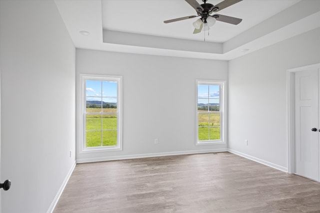 unfurnished room with plenty of natural light, light hardwood / wood-style floors, a tray ceiling, and ceiling fan