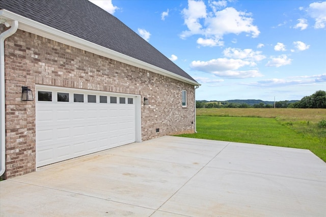 view of side of home with a rural view, a garage, and a lawn