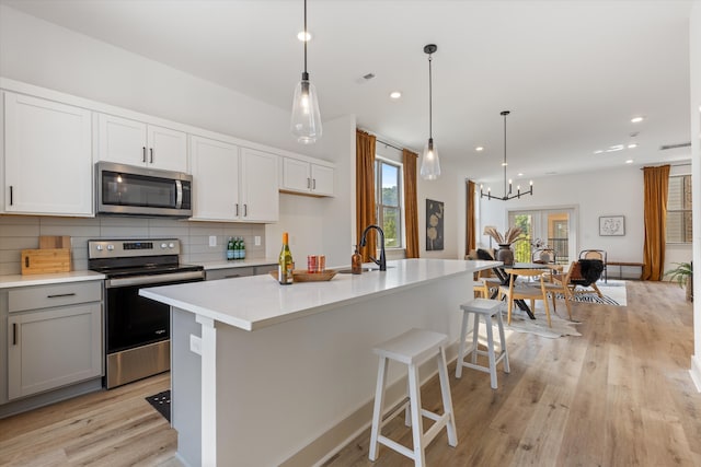 kitchen with an island with sink, decorative light fixtures, stainless steel appliances, and tasteful backsplash