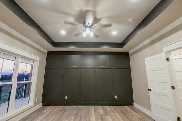 unfurnished bedroom with light hardwood / wood-style floors, ceiling fan, and a tray ceiling