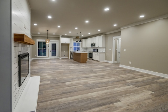 kitchen with ornamental molding, stainless steel appliances, a kitchen island, hanging light fixtures, and white cabinets