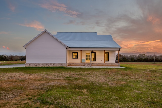 back house at dusk featuring a lawn and covered porch