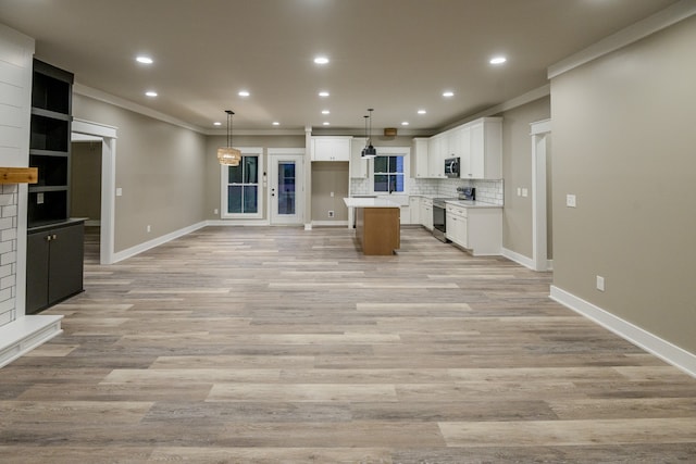 kitchen with ornamental molding, white cabinetry, appliances with stainless steel finishes, pendant lighting, and a center island