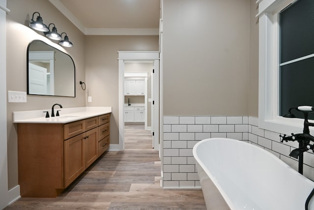 bathroom with hardwood / wood-style floors, vanity, and a relaxing tiled tub