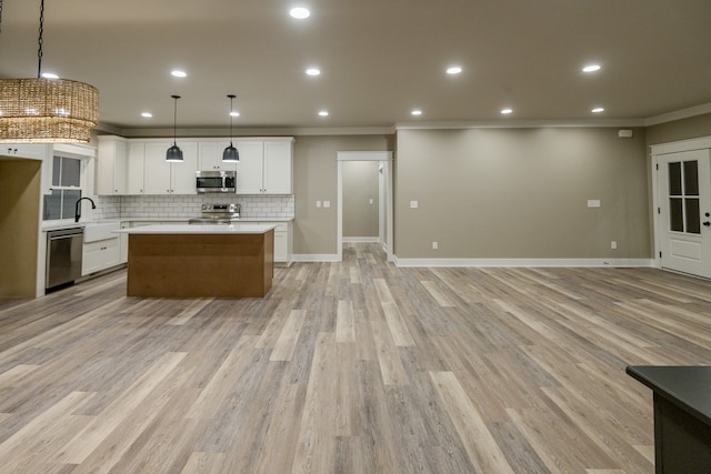 kitchen featuring crown molding, light wood-type flooring, white cabinetry, appliances with stainless steel finishes, and decorative light fixtures