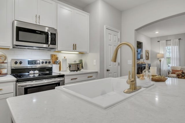 kitchen with appliances with stainless steel finishes, backsplash, white cabinetry, and sink