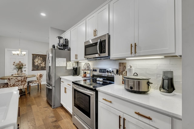 kitchen featuring hanging light fixtures, stainless steel appliances, an inviting chandelier, white cabinets, and hardwood / wood-style flooring