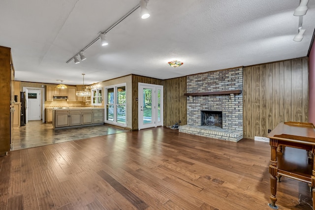 unfurnished living room featuring hardwood / wood-style flooring, a fireplace, wood walls, and rail lighting