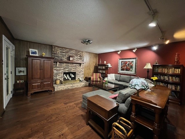 living room featuring rail lighting, dark hardwood / wood-style flooring, a fireplace, wood walls, and a textured ceiling