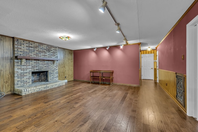 unfurnished living room featuring a fireplace, wood-type flooring, wooden walls, and track lighting