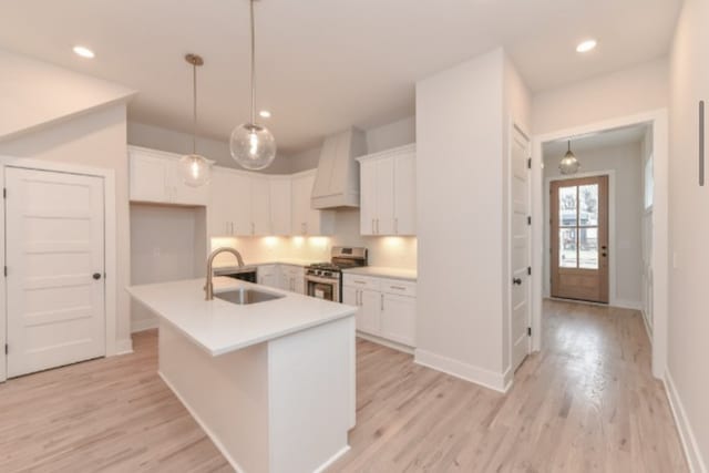 kitchen featuring light hardwood / wood-style flooring, a center island with sink, sink, stainless steel gas range, and white cabinetry