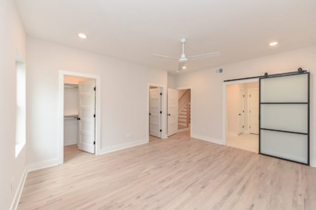 unfurnished bedroom with light hardwood / wood-style flooring, a closet, a barn door, and a walk in closet