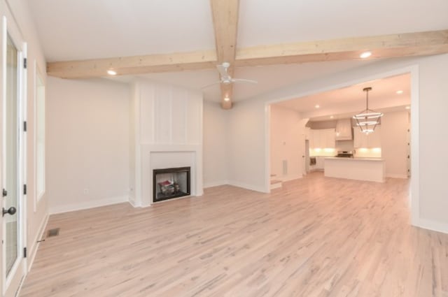 unfurnished living room featuring a large fireplace, light hardwood / wood-style floors, beam ceiling, and ceiling fan