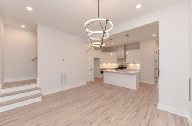 kitchen with hanging light fixtures, sink, a kitchen island with sink, white cabinetry, and light hardwood / wood-style floors