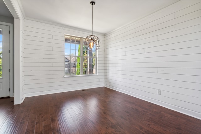 unfurnished dining area featuring ornamental molding, wood walls, dark hardwood / wood-style floors, and a notable chandelier