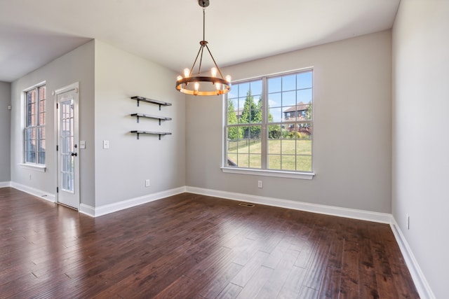 spare room with a chandelier and dark wood-type flooring