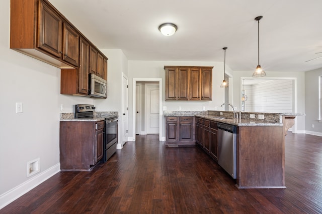 kitchen featuring light stone countertops, dark hardwood / wood-style floors, stainless steel appliances, sink, and decorative light fixtures