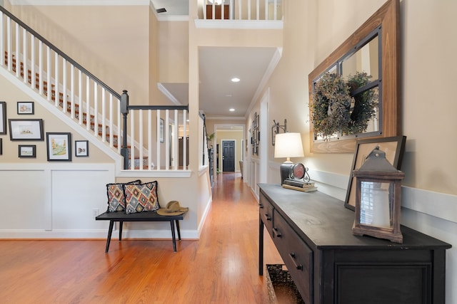 foyer entrance featuring a towering ceiling, crown molding, and light hardwood / wood-style flooring