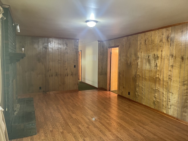 unfurnished room with hardwood / wood-style floors, a brick fireplace, and wooden walls