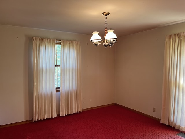 carpeted empty room featuring a notable chandelier