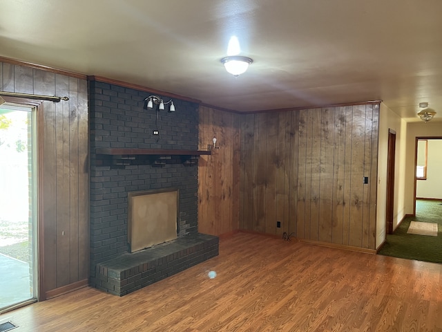 unfurnished living room featuring hardwood / wood-style floors, a brick fireplace, and wood walls