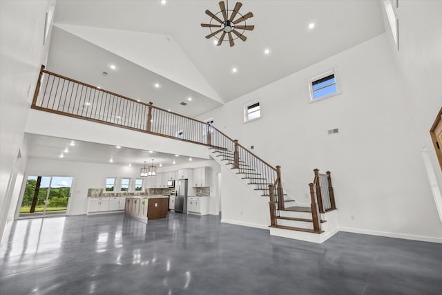 unfurnished living room with ceiling fan with notable chandelier and high vaulted ceiling