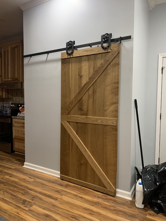 interior space featuring wood-type flooring, crown molding, a barn door, electric stove, and backsplash