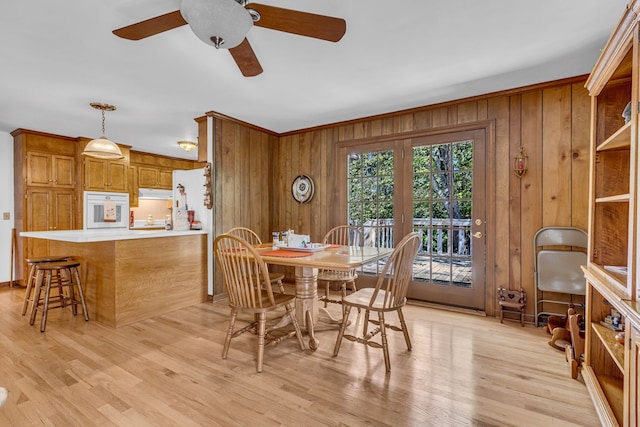 dining room with ornamental molding, light hardwood / wood-style flooring, wooden walls, and ceiling fan